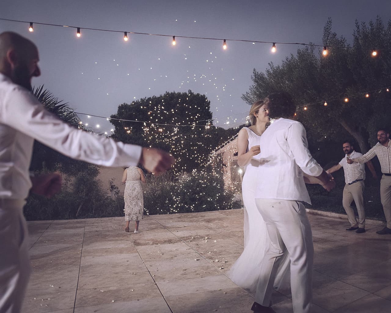 Guests dancing under string lights on an open-air floor at dusk
